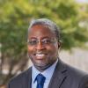 David Coaxum in formal photo, wearing a gray suit with light blue shirt and blue tie